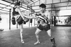 woman kicking thai pads in phuket with trainer muay thai