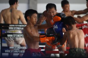 kids sparring trainer watching and teaching muay thai camp